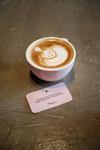 Classic Cafe Latte in a Pink Cup with a Protagonist message card saying BEHIND EVERY GREAT IDEA IS A MESSY TABLE AND A STRONG BREW 