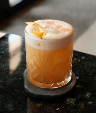 Main Character Sour Signature Cocktail in glass held in a hand